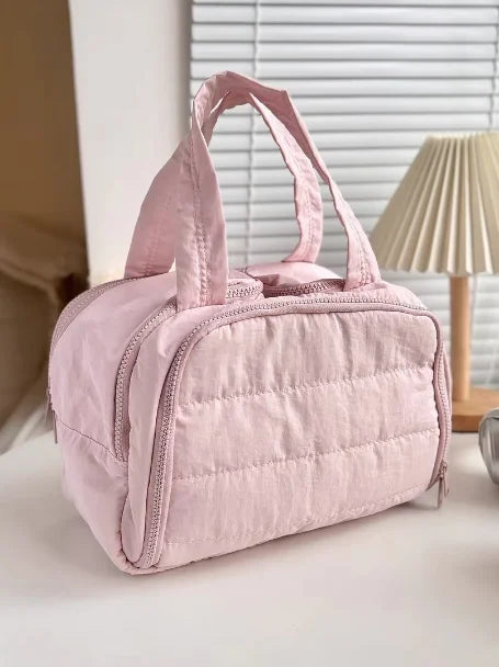 A soft pink quilted travel makeup bag with a wide opening is shown on a white surface.