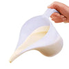 A hand is pouring a creamy white liquid from a white plastic measuring cup with a long spout.