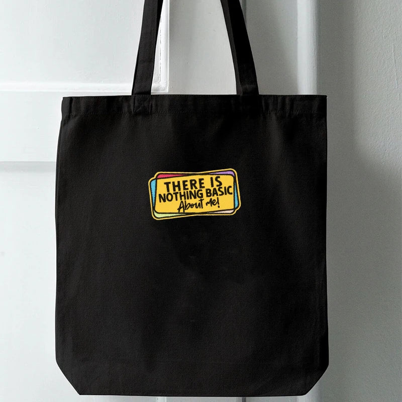 Black tote bag with an embroidered patch that reads There is nothing basic about me