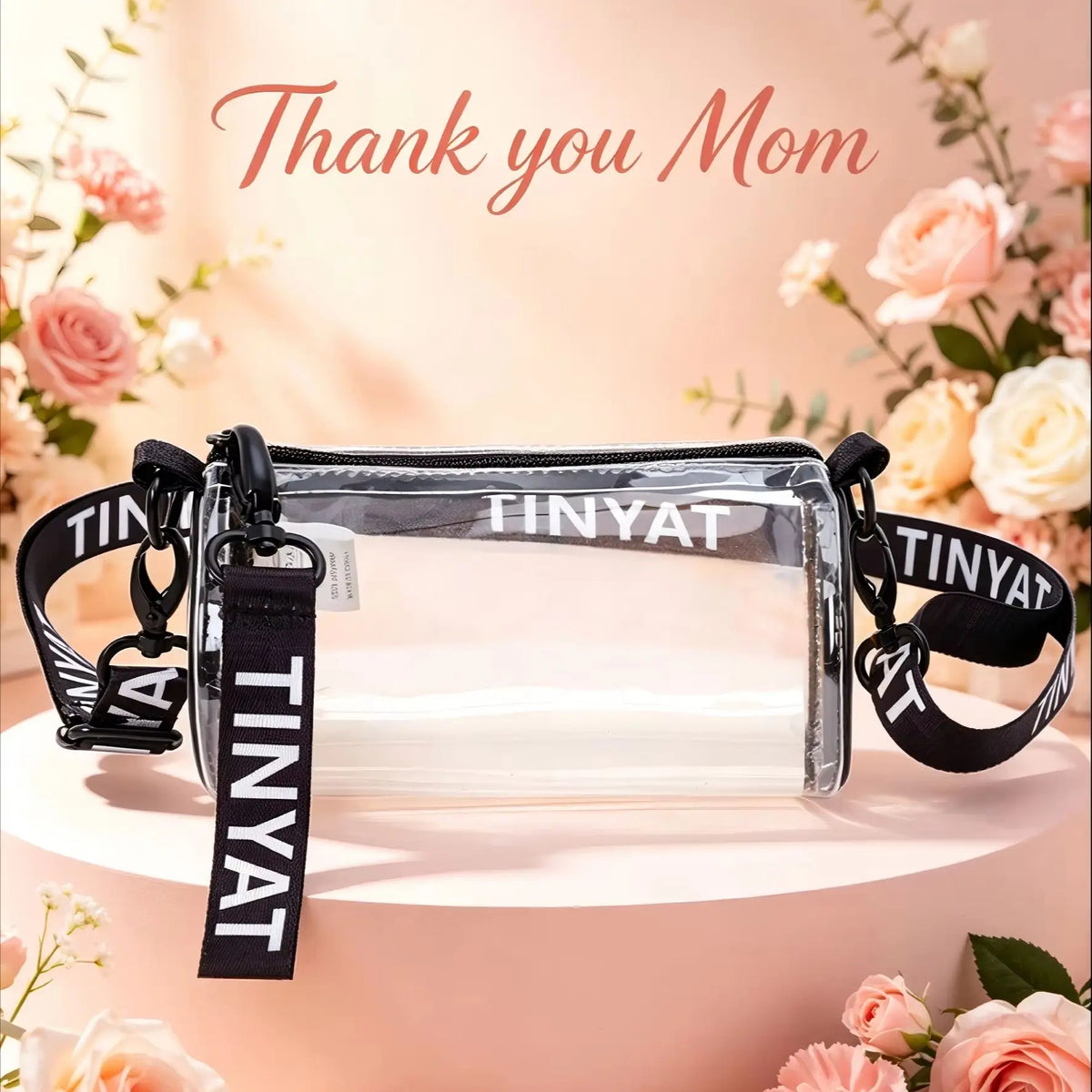A clear crossbody bag with a black adjustable strap displayed on a pink cake decorated with flowers.