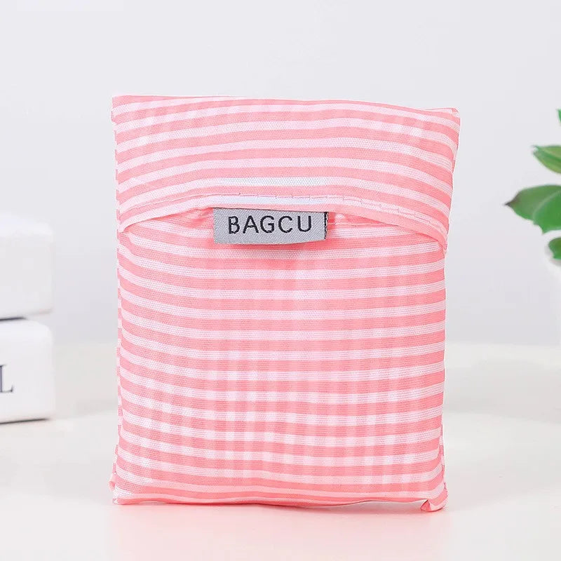 A pink and white striped foldable eco-friendly shopping bag with the brand name BAGCU visible on the front.