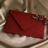 A deep red linen texture envelope with a gold sealing wax sticker rests on a beige silk fabric.