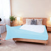 Light blue stretch-fit box spring cover displayed on a wooden bed frame with fluffy pillows.