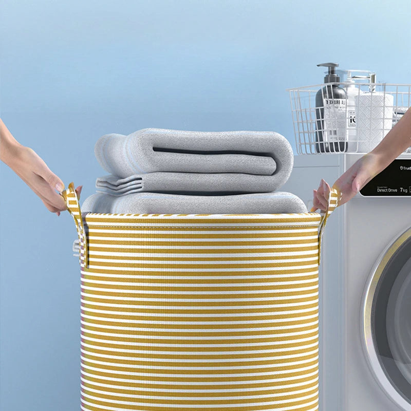 A yellow and white striped foldable laundry basket filled with folded gray towels, being placed near a washing machine.