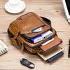 A brown genuine leather crossbody shoulder bag with multiple zippered compartments and attached accessories on a wooden surfa