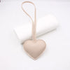 A light peach heart-shaped PU leather keychain with a cotton charm is displayed next to a rolled white tube.