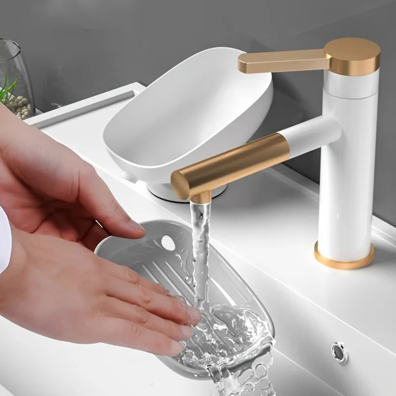 A hand is pouring water from a gold and white faucet into a leaf-shaped suction cup soap dish.