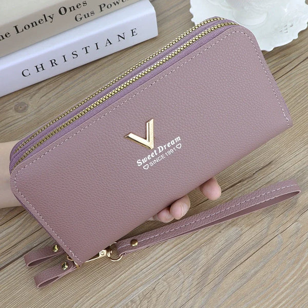 Portefeuille en cuir PU mauve à double zip avec logo or et sangle, posé sur une surface en bois.