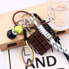 A gold-toned 8-ball metal keychain featuring a sleek black finish, next to a chocolate bar and leather cord.