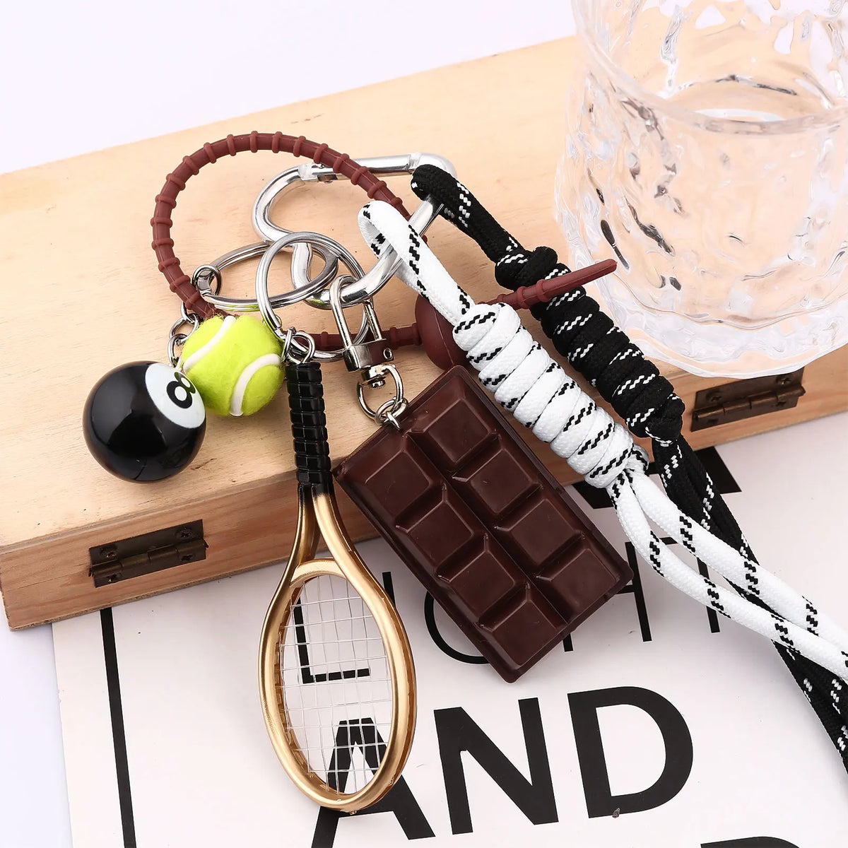 A gold-toned 8-ball metal keychain featuring a sleek black finish, next to a chocolate bar and leather cord.