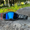 A pair of black motocross goggles with blue mirrored lenses resting on a large gray rock.