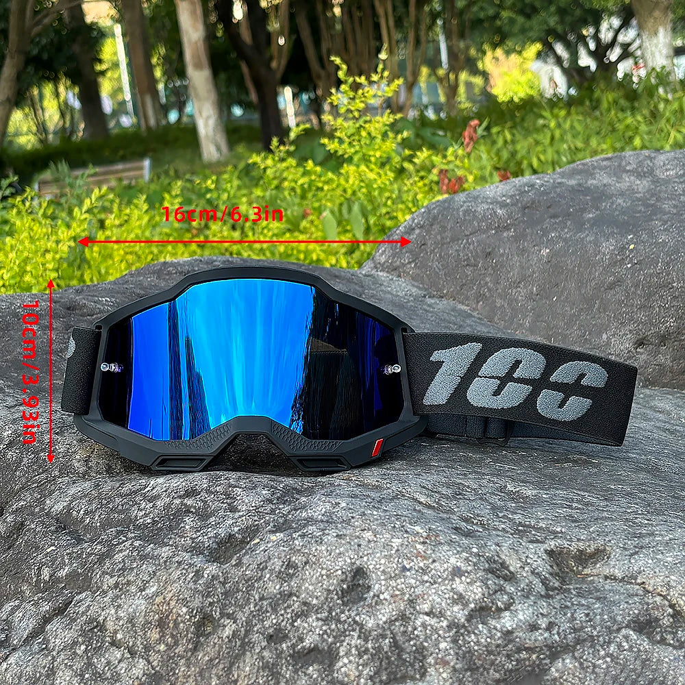 A pair of black motocross goggles with blue mirrored lenses resting on a large gray rock.