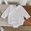 A white baby girl floral lace cotton romper with black polka dots lying on a wooden surface.