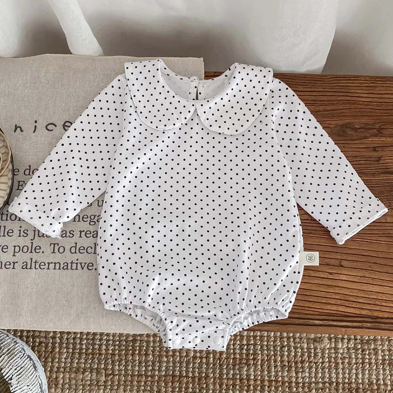 A white baby girl floral lace cotton romper with black polka dots lying on a wooden surface.
