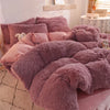 A pile of fluffy mauve mink velvet bedding, including a duvet cover and sheets, displayed on a bed.