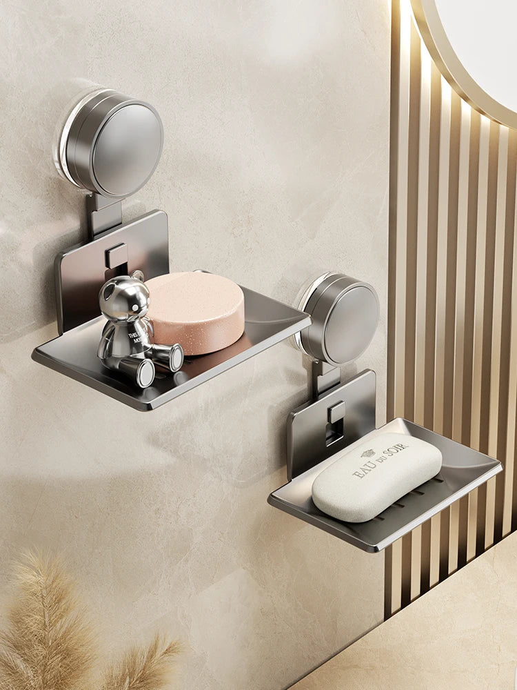 A wall-mounted soap dish with a suction cup dispenser and drain, featuring a silver metal finish.