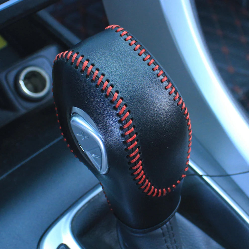Close-up of a black gear shift knob cover with red stitching mounted on a steering column.