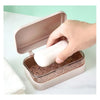 A hand opens a pink transparent soap dish with a drainage tray on a white surface.