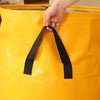 A hand is opening a bright yellow waterproof heavy-duty storage bag by pulling a black strap.
