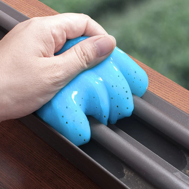 A hand is squeezing a bright blue reusable cleaning gel for car interiors and electronics.