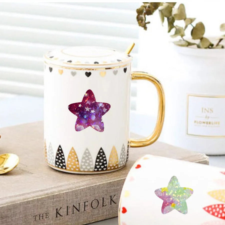 A white ceramic mug with a gold handle decorated with purple glitter stars and gold accents.