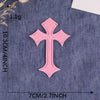 A single pink embroidered cross patch on a dark blue fabric background.