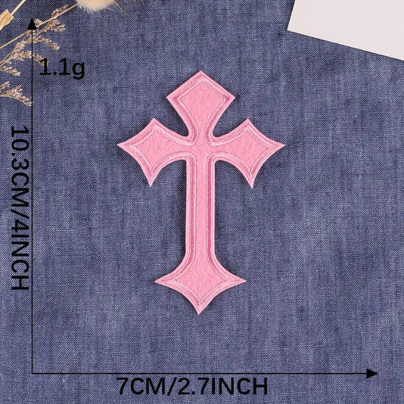 A single pink embroidered cross patch on a dark blue fabric background.