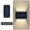 A black solar powered outdoor wall light with an upper and downward illumination pattern mounted on a textured wall.