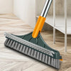 A green floor scrub brush with an orange handle and silver shaft is shown cleaning a wooden floor.
