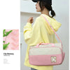 A woman wearing a yellow hoodie holds a pink and white patterned multifunctional crossbody diaper bag.
