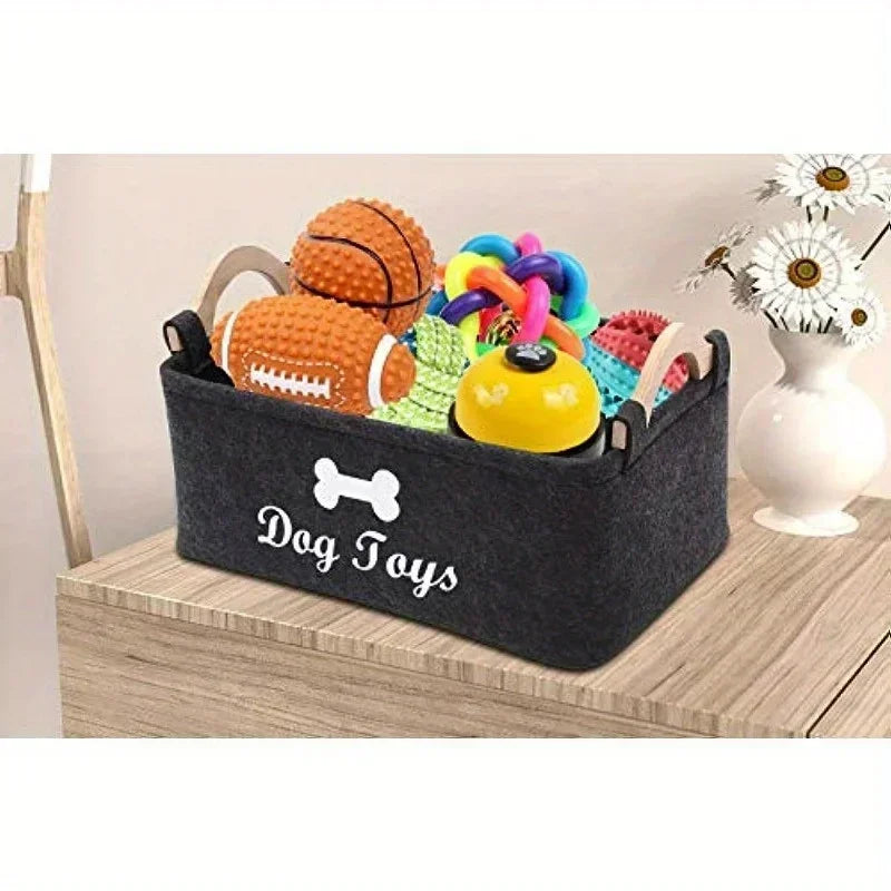A dark gray felt storage basket filled with various colorful dog toys including a ball and a bone shape.