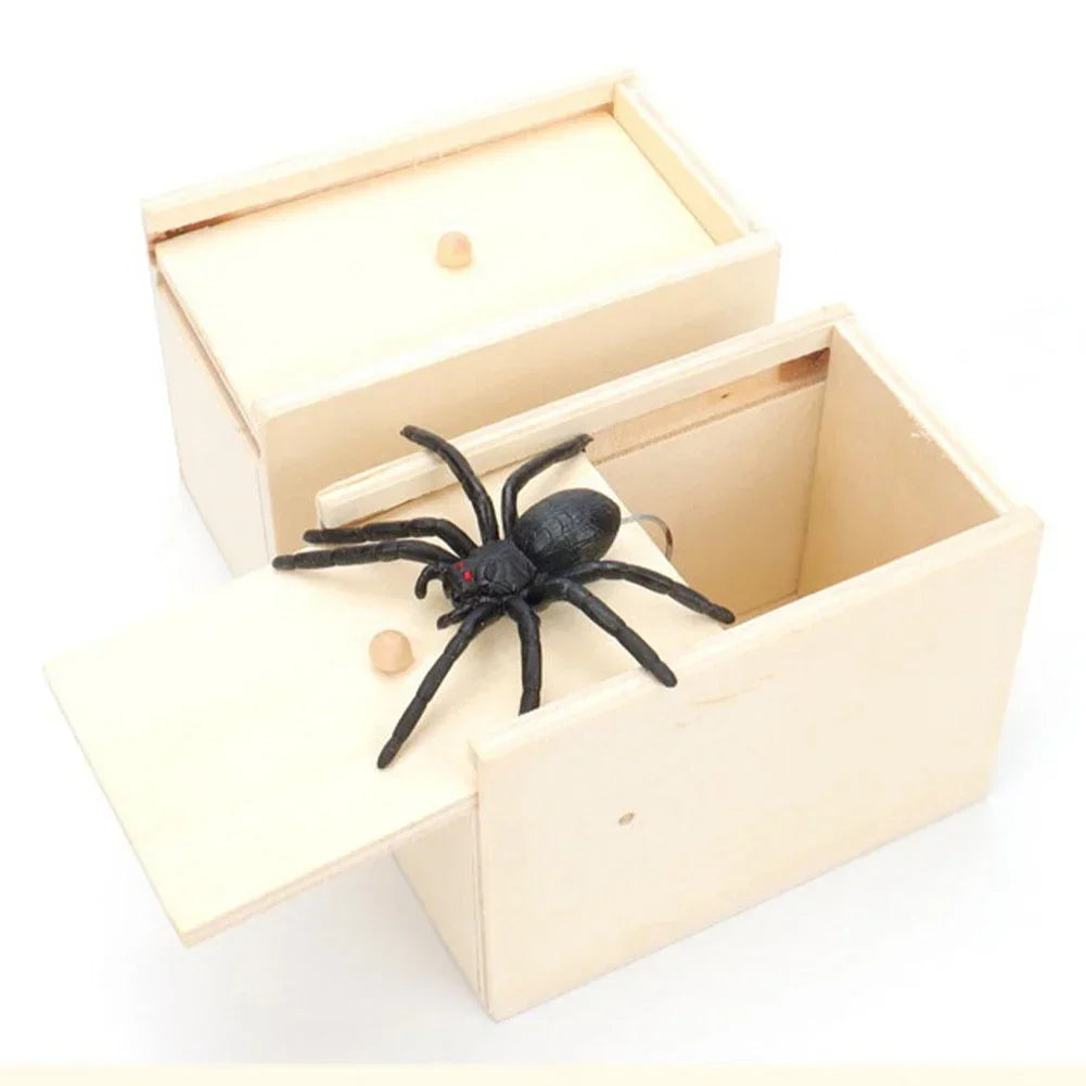 A light wooden box with a lid open, containing a black spider trick toy.