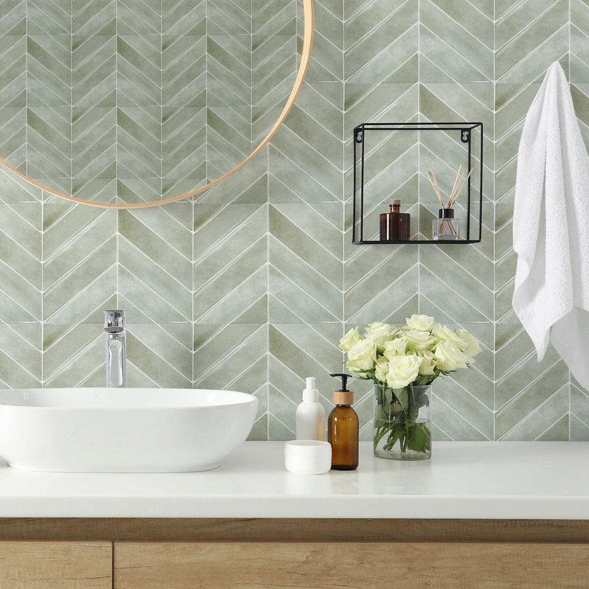 A bathroom counter with a white vessel sink, soap dispensers, and flowers against a green chevron tiled wall.