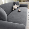 A gray stretch jacquard sofa cover featuring a textured fabric and a cream-colored decorative pillow.