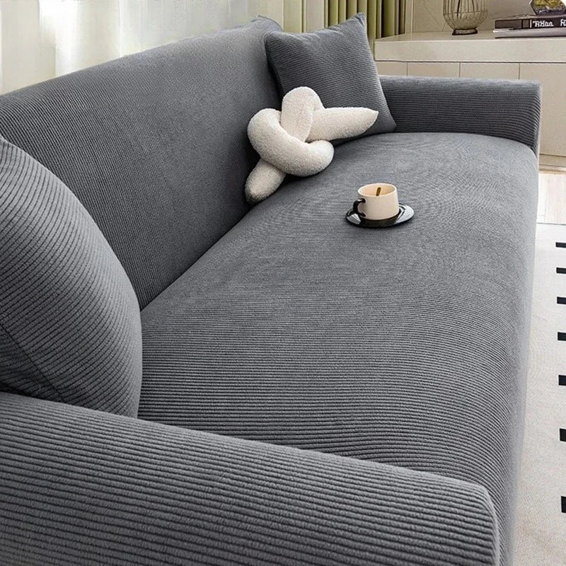 A gray stretch jacquard sofa cover featuring a textured fabric and a cream-colored decorative pillow.
