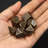 A hand holds a set of bronze metal polyhedral dice used for tabletop role-playing games