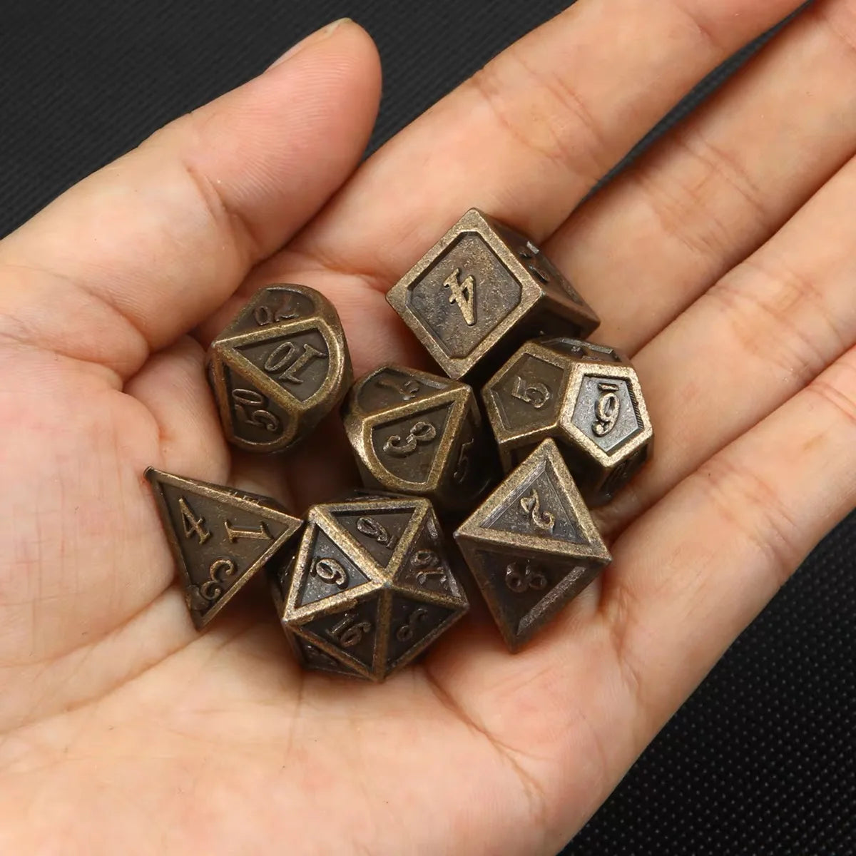 A hand holds a set of bronze metal polyhedral dice used for tabletop role-playing games