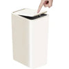 A hand is lifting the lid of a white pop-up slim trash can.