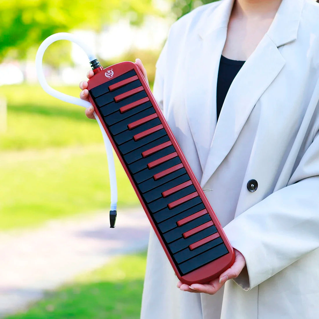 A person holds a red 32-key melodica instrument with a case and mouthpieces outdoors.