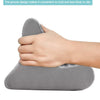 A hand is holding a gray, contoured pillow designed as a grip for an adjustable comfort tablet and phone stand.