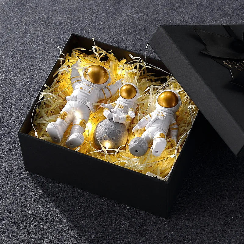 A black box contains three handcrafted astronaut figurine resin spaceman desk decor figures surrounded by yellow wispy materi
