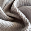 A close-up of a set of four light beige pure cotton waffle weave towels folded and draped.