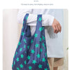 A dark blue shopping bag with a widened shoulder strap featuring green stars, being carried by a person.