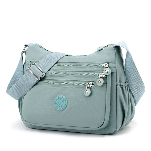 A light blue waterproof nylon crossbody bag with a flap and zippered pockets.