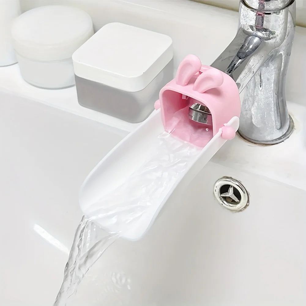 A pink rabbit-themed anti-splash faucet extender is shown dispensing water from a sink faucet.