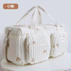 A cream-colored embroidered cotton diaper bag featuring a quilted pattern and bear and floral designs.