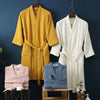A display of three lightweight cotton waffle robes in yellow, white, and blue hanging against a dark blue wall.