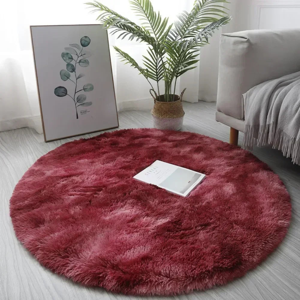 A round, deep red shaggy area rug placed on a light gray floor next to a potted plant and framed artwork.
