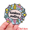 A round embroidery patch featuring floral designs and the text kindness matters on a light blue background.
