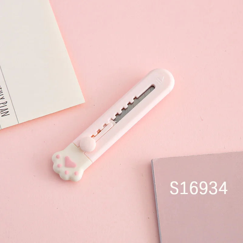 Weiiges Mini-Katzenzoll-Werkzeugmesser mit rosa Pfotenformgriff auf rosa Hintergrund.